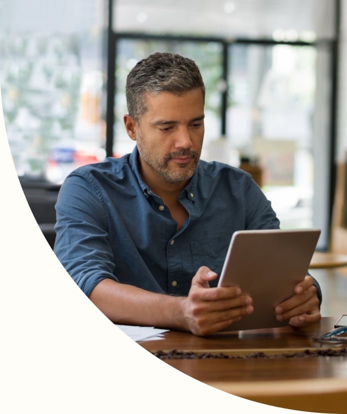 White male sitting at table looking at his tablet. 